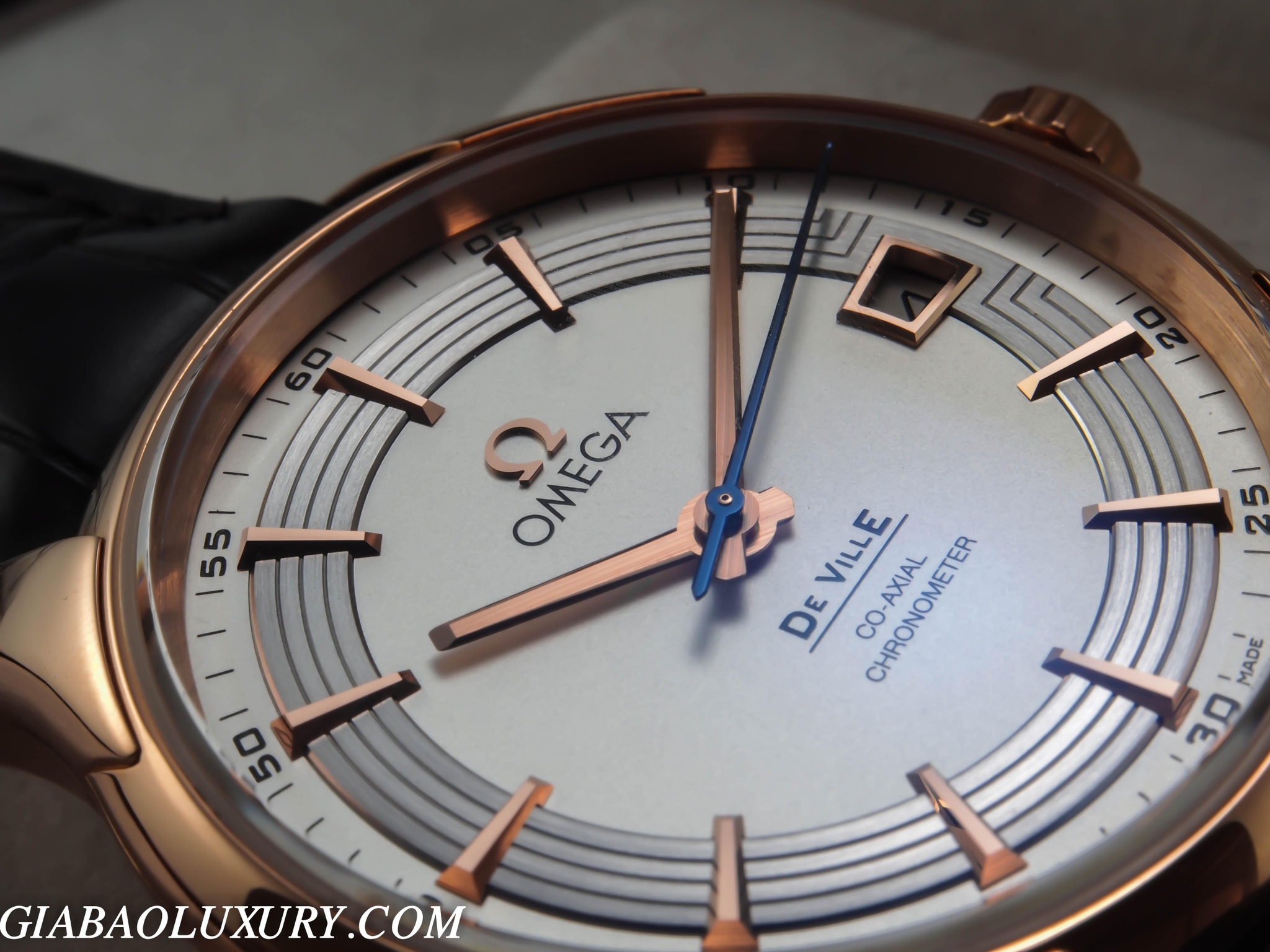Cận cảnh mặt số Omega De Ville Hour Vision với kim giờ phút vàng hồng, kim giây xanh và cửa sổ lịch ngày
