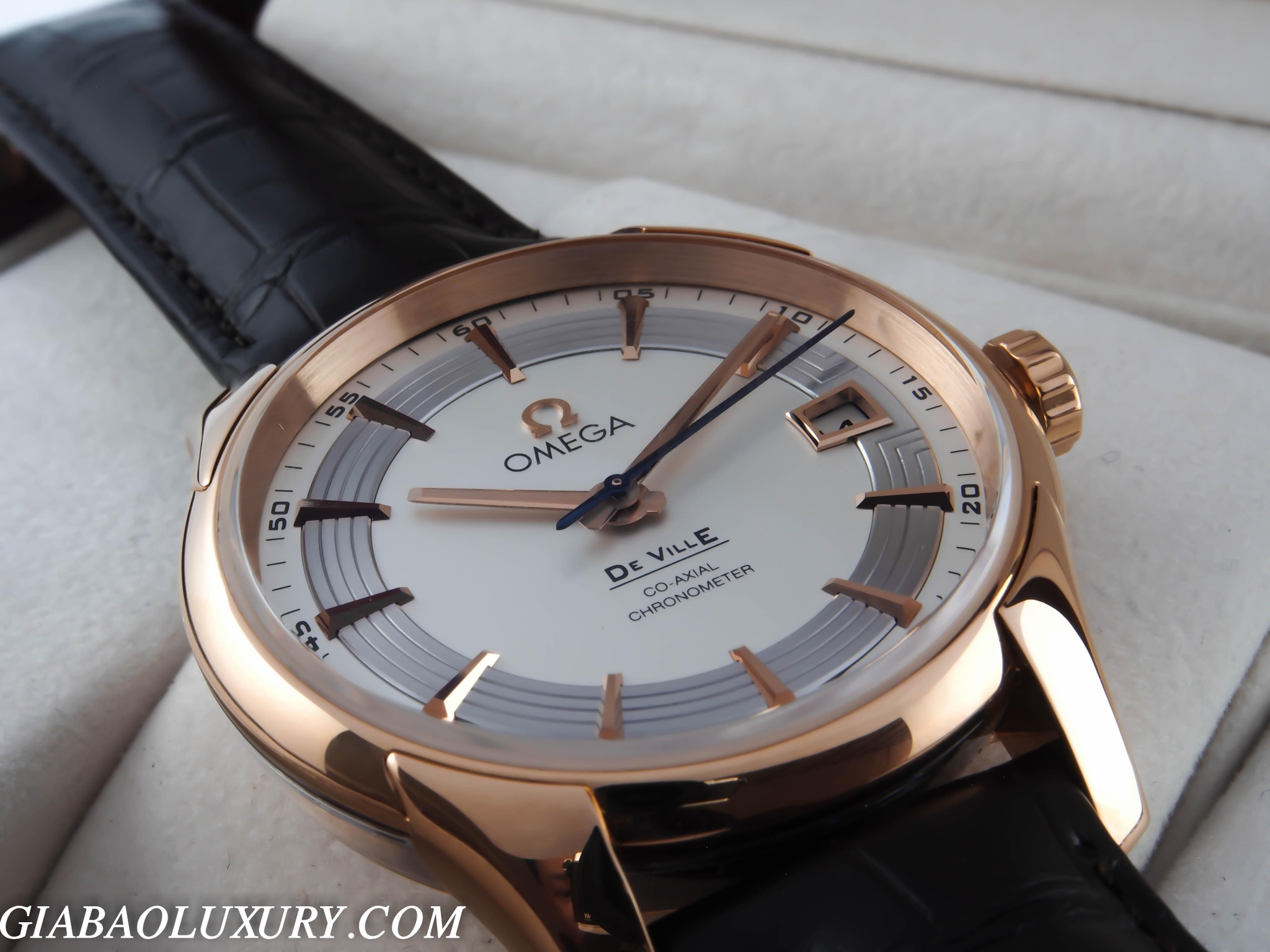 Omega De Ville Hour Vision vỏ vàng hồng mặt số bạc trên dây da đen đặt trên gối trưng bày