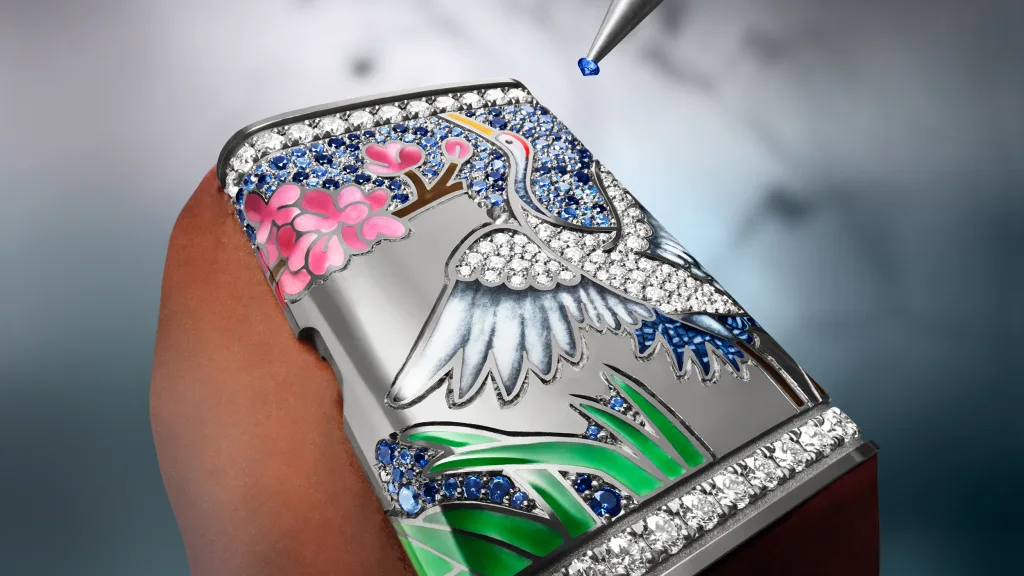 Cận cảnh phần vỏ Sakura với hoa hồng, chim hạc, đá xanh và nhíp giữ một viên sapphire